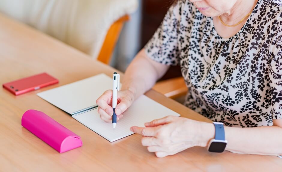 高齢の女性がノートに何かを書いている写真